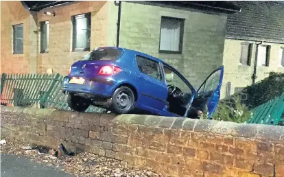  ??  ?? The car on top of the garden wall where it was left by its driver after a smash which wrecked a metal fence