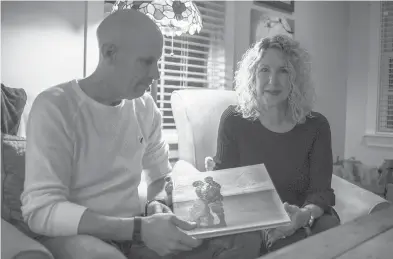  ?? COURANT FILE PHOTO ?? Peter and Lisa Marshall hold their wedding album and sit for a portrait in their living room of their home on Dec. 6, 2019, in Andover. The couple remarried in 2021, two years after Peter was diagnosed with early-onset Alzheimer’s.