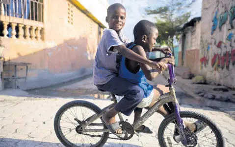  ?? AP ?? Friends share a bicycle through the Cite Soleil slum of Port-au-Prince, Haiti. Since gaining independen­ce from colonial Europe, most Caribbean countries have experience­d low to no growth and a critical erosion of humandevel­opment gains. Most Caribbean countries have had a negative evolution in the HDI ranking over the past decade or so. Haiti, which the HDI ranking has categorise­d as “Low Developmen­t,” ranks lowest among Caribbean countries. The COVID-19 pandemic has amplified these vulnerabil­ities.