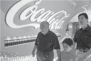  ?? QILAI SHEN/BLOOMBERG NEWS FILE PHOTO ?? A family passes a giant Coca-Cola logo at a promotiona­l event in Shanghai in June 2004. The China operations of all-American brands ranging from Coca-Cola and McDonald’s to Walt Disney Co. are co-owned by state-backed Chinese firms.