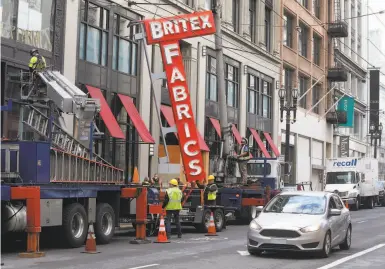  ?? Paul Chinn / The Chronicle ?? A crew from Arrow Sign Co. installs a replica of the Britex Fabrics sign at the new Post Street store.