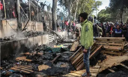  ??  ?? Refugees and migrants stand near a burnt area after a fire broke out in Moria camp on the island of Lesbos. Photograph: Manolis Lagoutaris/AFP via Getty Images