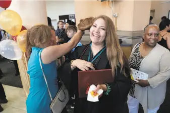  ?? Carlos Avila Gonzalez / The Chronicle ?? Tany Rios Castro gets help straighten­ing out her hair from her mother, Rocio Castro Mendoza, after the graduation ceremony for the Working Scholars program sponsored by Study.com.