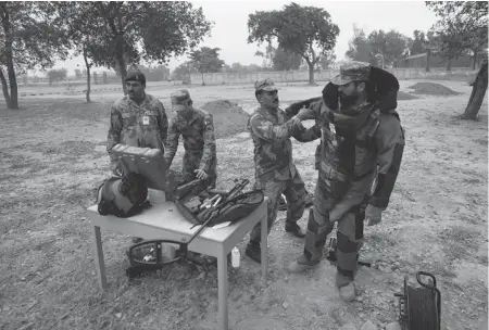  ?? PHOTOS: ANJUM NAVEED/ THE ASSOCIATED PRESS ?? A Pakistani soldier helps his colleague to put on a bomb suit for a training session in defusing bombs in Risalpur.