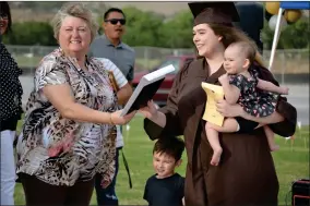  ??  ?? After arriving on a trolley filled with family and firends, Zoie Jones grabs her diploma during the drive-thru gradaution ceremony held at Butterfiel­d Charter School on Friday evening.