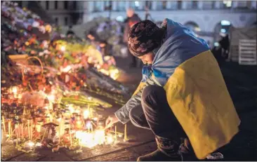  ?? BULENT KILIC/ AGENCE FRANCE- PRESSE VIA GETTY IMAGES ?? A woman lights a candle early Monday at a makeshift memorial to anti- government protesters killed in the past weeks’ clashes with riot police in Kiev. President Viktor Yanukovych has reportedly fled the capital.