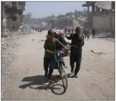  ?? Fatima Shbair/Associated Press ?? Palestinia­ns walk through the destructio­n in the wake of an Israeli air and ground offensive Monday in Khan Younis, southern Gaza Strip.