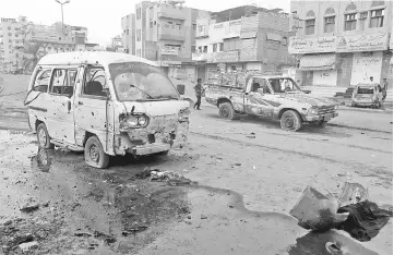  ??  ?? People walk past damaged cars at the entrance of Al-Thawra hospital after an air strike.