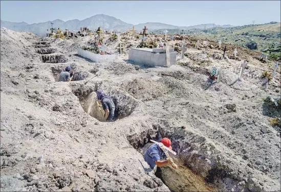  ?? Photograph­s by Marcus Yam Los Angeles Times ?? WORKERS prepare graves at Municipal Cemetery No. 13 in Tijuana. Those who bury the dead wear protective suits and spray themselves down with disinfecta­nt.