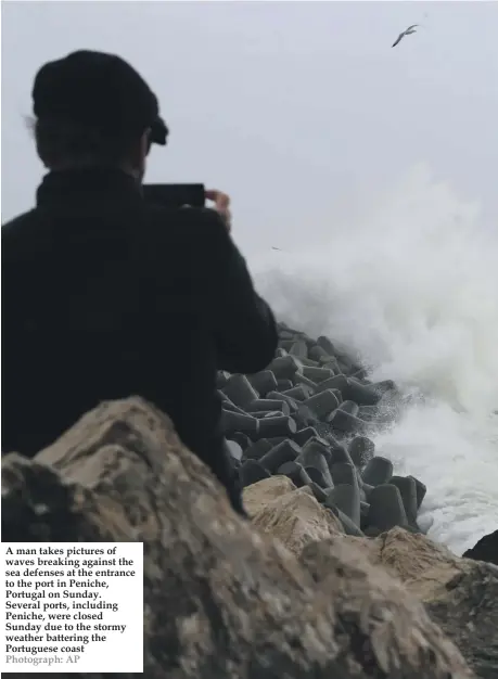  ?? Photograph: AP ?? A man takes pictures of waves breaking against the sea defenses at the entrance to the port in Peniche, Portugal on Sunday. Several ports, including Peniche, were closed Sunday due to the stormy weather battering the Portuguese coast