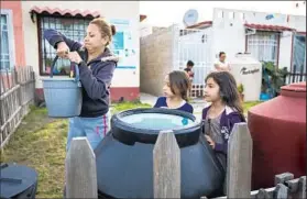  ?? Brian van der Brug Los Angeles Times ?? ANAHID FIGUEROA, 35, hoists a bucket of water, delivered by truck, in her postagesta­mp frontyard with her daughter Valeria, 8, and friend Aria Merlos, 7, right.