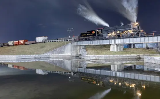  ?? Walter Scriptunas II photo, Sol Tucker lighting ?? Perched high on the dike that forms the inlet from Wills Creek and the Chesapeake & Ohio Canal in downtown Cumberland, Md., No. 1309 and its 11-car photo freight with caboose poses in a night photo session on Feb. 26, 2022.