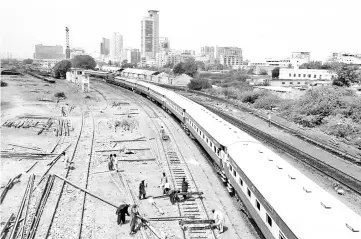  ?? – Reuters photo ?? A passenger train moves past labourers working on a railway track along City Station in Karachi, Pakistan. After lengthy delays, an US$8.2 billion revamp of a colonial-era rail line snaking from the Arabian Sea to the foothills of the Hindu Kush has become a test of Pakistan’s ability to rethink signature Chinese ‘Silk Road’ projects due to debt concerns.