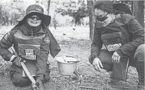  ?? KAYLEB LEE ?? Khamsone Sirimanivo­ng, right, talks with a deminer in southern Laos last month as she digs up bomb fragments found by a metal detector.