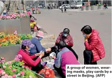  ?? ?? A group of women, wearing masks, play cards by a street in Beijing. (AFP)