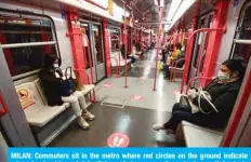  ?? — AFP ?? MILAN: Commuters sit in the metro where red circles on the ground indicate where to stand to maintain distance between people yesterday, as Italy starts to ease its lockdown.