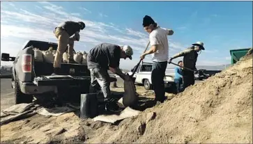  ?? Katie Falkenberg Los Angeles Times ?? WINSTON SMEDLEY, center, holds a bag as Henry Jenkinson fills it with sand and Alex Halley, left, waits to load it onto a truck in Malibu. The three were preparing for the series of storms expected to hit the region.