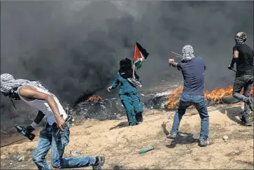  ?? Marcus Yam Los Angeles Times ?? SHROUDED by smoke from burning tires, Palestinia­n protesters aim slingshots at the border fence separating Israel and the Gaza Strip on Friday. Some demonstrat­ors are threatenin­g to breach the border this week.