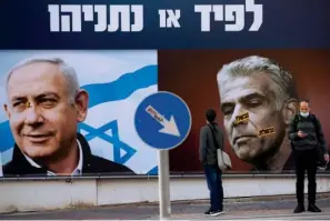  ?? The Associated Press ?? ■ In this March 14 file photo, people stand in front of an election campaign billboard for the Likud party showing a portrait of its leader Prime Minister Benjamin Netanyahu, left, and opposition party leader Yair Lapid, in Ramat Gan, Israel. Israel’s President Reuven Rivlin has tapped Lapid to form a new government, a step that could lead to the end of Netanyahu’s lengthy rule.