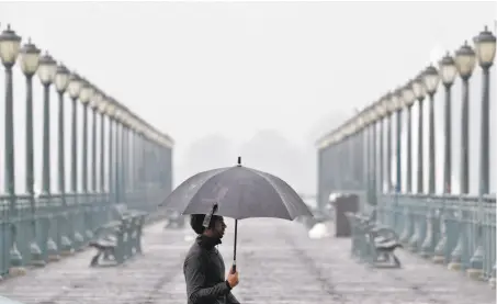  ?? Carlos Avila Gonzalez / ?? A man carrying an umbrella for protection from driving rain walks along the Embarcader­o in S.F., as a fierce storm dropped several inches of rain in November. A new Stanford study blames global warming for extreme weather becoming commonplac­e.