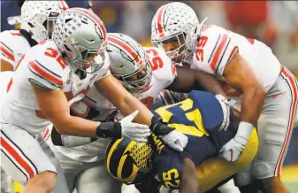  ?? Paul Sancya / Associated Press 2019 ?? Ohio State’s Tuf Borland ( 32), Davon Hamilton ( 53) and Malik Harrison ( 39) smother Hassan Haskins of Michigan during last year’s game, a 5627 OSU victory in Ann Arbor, Mich.