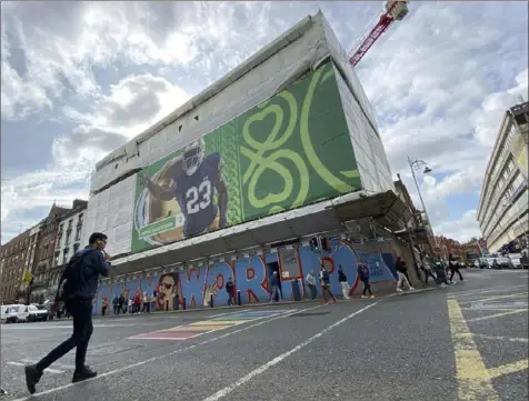  ?? Kenneth Maguire/Associated Press ?? A pedestrian crosses Dame Street below a giant Notre Dame football placard Friday in Dublin. Notre Dame will play Navy at Aviva Stadium on Saturday when a portion of Dame Street will be closed to traffic to become a fan zone. Close to 40,000 internatio­nal fans are expected in Ireland’s capital.