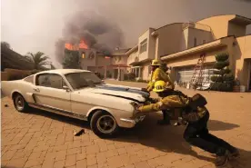  ??  ?? Firefighte­rs push a car from a garage as a home burns in Malibu. Photograph: Ringo HW Chiu/AP