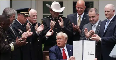  ?? GETTy IMaGES ?? ‘EQUALITY FOR ALL’: Surrounded by members of law enforcemen­t, including Bristol County Sheriff Thomas Hodgson, fourth from left, President Trump holds up an executive order he signed that will track bad cops.