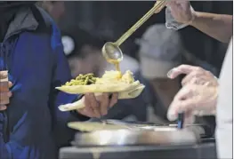  ??  ?? A volunteer puts gravy on a plate of food for a guest at the dinner. The meal is open to anyone, according to Christina Rajotte, director of developmen­t and marketing for Equinox.