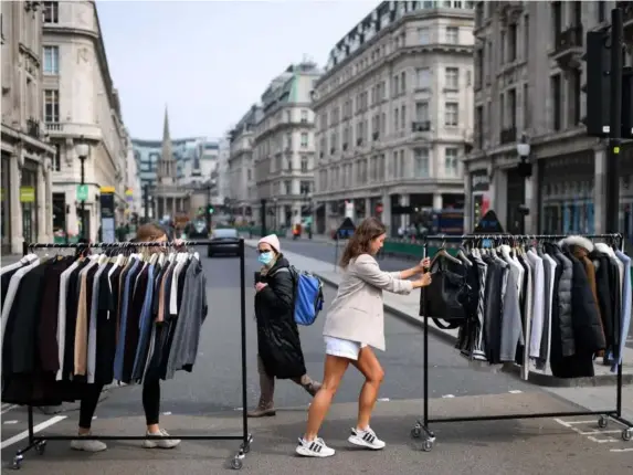  ?? (AFP via Getty) ?? Retail workers move rails of clothes between stores on Oxford Street ahead of reopening yesterday