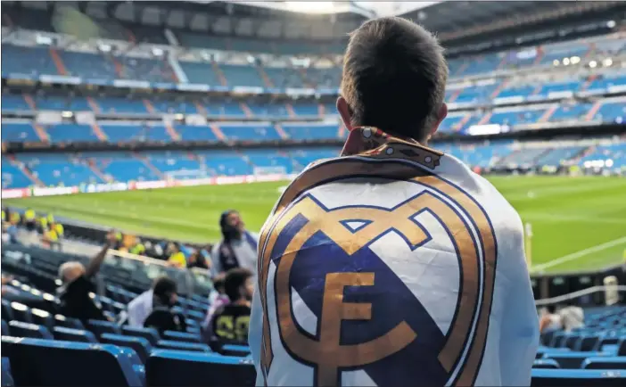  ??  ?? Un aficionado envuelto en una camiseta del Real Madrid contempla el Santiago Bernabéu, prácticame­nte vacío, antes de un partido de Champions.