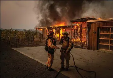  ?? JOSH EDELSON — AFP VIA GETTY IMAGES ?? As powerful winds fan wildfires, firefighte­rs discuss how to approach the scene as a house burns near grapevines in the Kincade Fire in Healdsburg on Sunday.