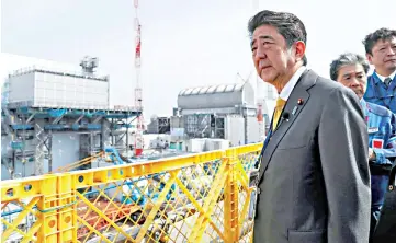  ?? — AFP photo ?? Abe visits the Tepco Fukushima Dai-ichi nuclear power plant as he stands in front of the reactor number 2 (left) and number 3 (right) buildings in Okuma.