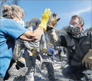  ?? Photograph­s by Mel Melcon Los Angeles Times ?? TREVOR QUIRK, right, high-fives Leona Mote as volunteers sift through the rubble of Mote’s home near Ojai. She lost her husband of 54 years in October, then lost the home they had shared to the Thomas fire.