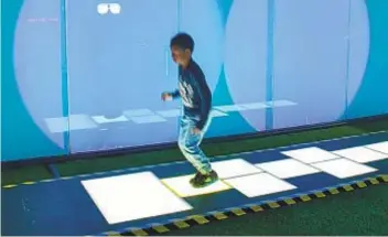  ?? FLEET SCIENCE CENTER PHOTOS ?? A child jumps across an illuminate­d hopscotch board in the 1980s room (also pictured at top) of the Fleet Science Center’s new “Flashback” exhibition.