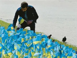  ?? SERGEI SUPINSKY/GETTY-AFP ?? A man sticks small Ukrainian flags carrying the names of servicemen killed in the war against Russia into a plot of grass Wednesday in the capital of Kyiv.