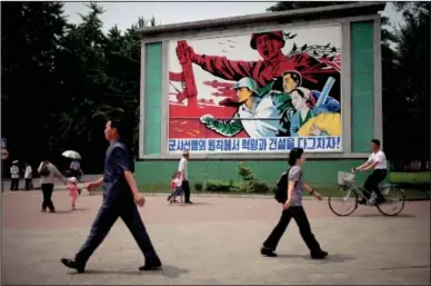  ?? AP photo ?? People walk past a roadside propaganda billboard promoting the “military first” policy and a boost to build the country’s economy in Pyongyang, North Korea, on Sunday. North Korea’s top governing body on Sunday proposed high-level nuclear and security...