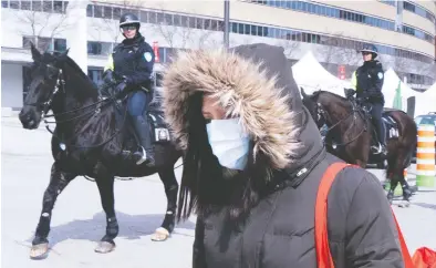  ?? PAUL CHIASSON / THE CANADIAN PRESS ?? A woman walks past members of the Montreal Police as she arrives at a walk-in COVID-19 test clinic on Wednesday.