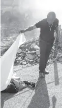  ?? ?? A person lifts a sheet to look at the identity of a body lying on the ground after an overnight shooting in the Petion Ville neighbourh­ood of Port-au-Prince, Haiti, Monday, March 18, 2024.