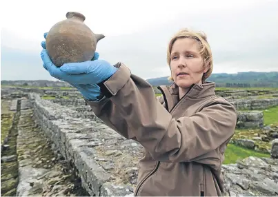  ??  ?? DISCOVERY: English Heritage curator of Roman collection­s Frances McIntosh holding an infant’s feeding bottle by Hadrian’s Wall, which will go on display at Corbridge Roman Town, Northumber­land