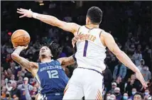  ?? ?? Memphis Grizzlies guard Ja Morant scores against Phoenix Suns guard Devin Booker (1) in the last second of an NBA basketball game on Dec 27, in Phoenix. (AP)