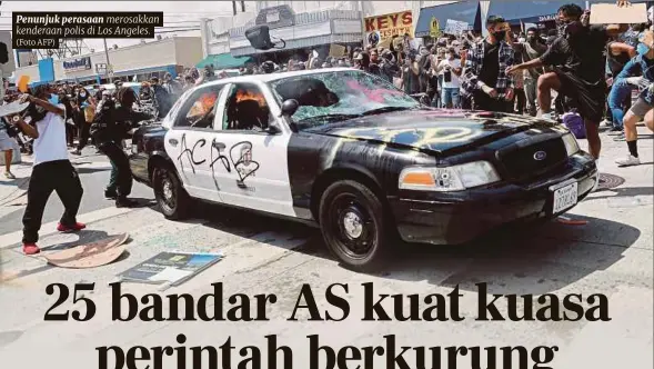  ?? (Foto AFP) ?? Penunjuk perasaan merosakkan kenderaan polis di Los Angeles.