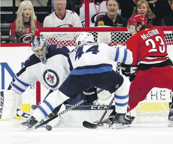  ?? KARL B DEBLAKER/THE ASSOCIATED PRESS ?? Winnipeg Jets goaltender Connor Hellebuyck keeps his eyes on the puck as Jets defenceman Josh Morrissey and Carolina Hurricanes winger Brock McGinn battle for space in the crease in the first period Sunday in Raleigh, N.C. The Jets won 3-2.