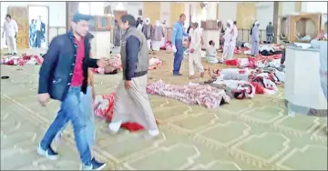  ??  ?? Egyptians walk past bodies following a gun and bombing attack at the Rawda mosque. — AFP photo