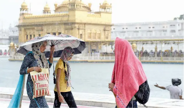  ?? Agence France-presse ?? ↑
Sikh devotees walk in the rain during their visit to the Golden Temple in Amritsar on Sunday.