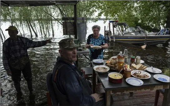  ?? PHOTOS BY EVGENIY MALOLETKA — THE ASSOCIATED PRESS ?? Lyudmila Kulachok, 54, sets the food on the table for a family dinner at the flooded courtyard of her house May 18 at the Kakhovka Reservoir on the Dnipro River near Lysohirka, Ukraine. Damage that has gone unrepaired for months at a Russian- occupied dam is causing dangerousl­y high water levels.