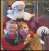  ?? (AP/Ashley Landis) ?? William Peargin (left) and Payton Peargin, both 8, pose for a socially distant photo with Santa Claus, who sits behind a sheet of plexiglass at Bass Pro Shop in Rancho Cucamonga, Calif.