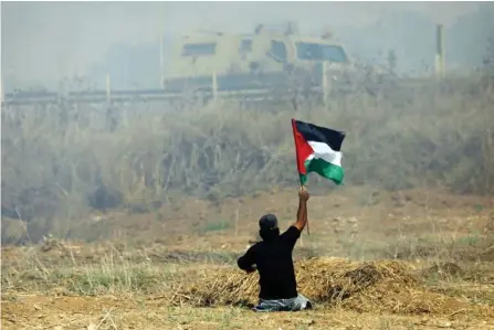  ??  ?? Handicappe­d Palestinia­n demonstrat­or Ibrahim Abu Thurayeh waving a Palestinia­n flag during clashes with Israeli soldiers following a protest against the blockade on Gaza City. (AFP/file)