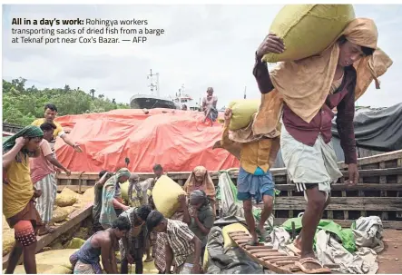  ?? — AFP ?? All in a day’s work: Rohingya workers transporti­ng sacks of dried fish from a barge at Teknaf port near Cox’s Bazar.