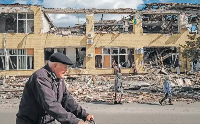  ?? Picture: AFP ?? SHELLED. People walk past a destroyed building in Kupiansk, Kharkiv region, on Monday mid the Russian invasion of Ukraine. In the northeaste­rn town of Kupiansk, which was recaptured by Ukrainian forces, clashes continued with the Russian army entrenched on the eastern side of the Oskil river.